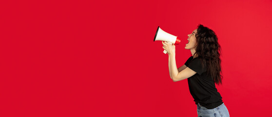 Young Caucasian woman with loudspeaker posing isolated on red background. Flyer