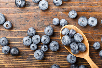 Fresh blueberries in a wooden spoon. The berries are scattered on a wooden table. Vegan and vegetarian concept.