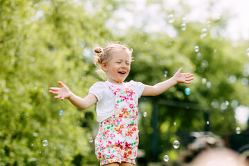 A cheerful girl catches soap bubbles with her hands and laughs. Happy childhood, summer time