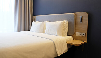 Close-up fragment of bedroom with empty bedside table, reading lamp and a USB socket in modern interior​ design home or hotel. Soft pillow and blanket, stylish comfortable furniture. 