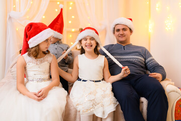 Fototapeta premium family portrait - parent and children in home interior decorated with holiday lights and gifts, dressed in santa hat for new year celebration