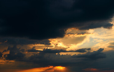 beautiful sunset sky, bright sun and dark silhouette of clouds as a background