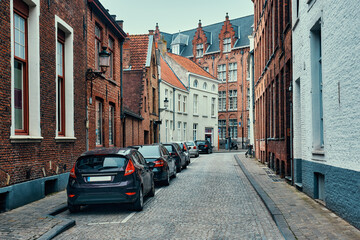 Fototapeta na wymiar Brugge street with cobblestone road with parked cars and old medieval houses. Bruges, Belgium