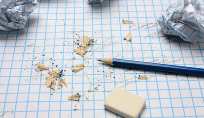 crumpled paper balls and a sharpened wooden pencil with shavings on a checkered paper sheet