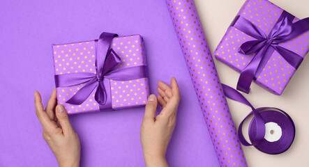 two female hands are holding purple gift box on paper background, concept of congratulations on birthday