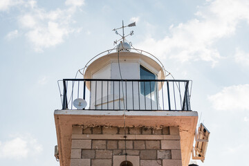 The stone brick and metal dome of the lighthouse with the directions of the world. White arrows in a cloudy sky designating north, south, east and west.