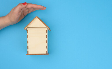 Obraz na płótnie Canvas female hand over wooden miniature model house on blue background. Real estate insurance concept, environmental protection