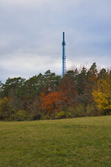 Obraz premium Blauer Funkturm auf dem Landgrafen hinter herbstlichem Mischwald und grüner Wiese, Jena, Thüringen, Deutschland