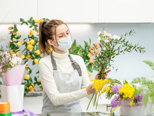 Young Woman wearing medical protective face mask cuts flowers at floral shop during the coronavirus epidemic