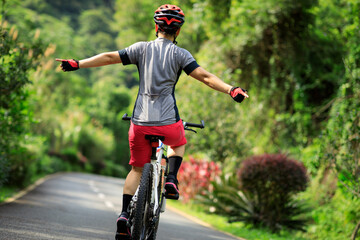 Woman no handed cycling on tropical park trail in summer