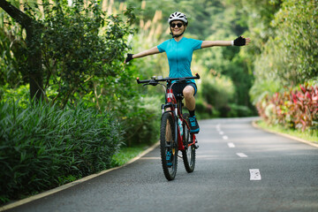 Woman no handed cycling on tropical park trail in summer