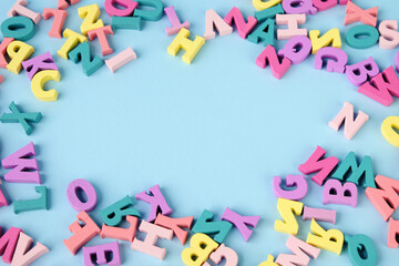 Lots of multicolored wooden letters scattered on a blue background. Copy space in center. - obrazy, fototapety, plakaty