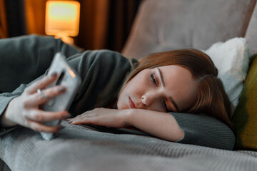 Obraz na płótnie Canvas Sad teenage girl suffering from insomnia surfing Internet or chatting using smartphone at night lying on bed. Depression Internet addiction. Young woman depression
