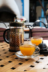 Close up view on french press and cups with sea buckthorn tea on the table.