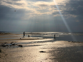 Unusual evening light on the beach at low tide in the sea with human silhouettes