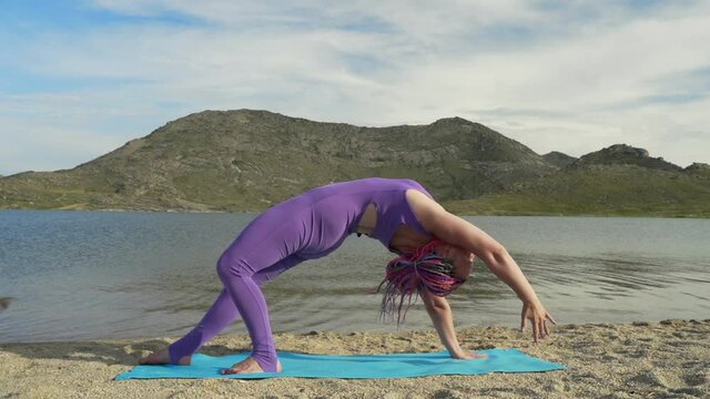 Young woman doing yoga poses, having training session on the lake shore. Sunrise