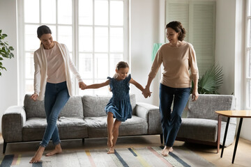 Smiling three generations of Caucasian women relax together in living room having fun on family leisure weekend. Happy small girl child with mother and grandmother dance at home, rest and play.