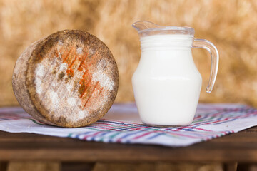jug of milk and head of cheese on table in barn against background of hay