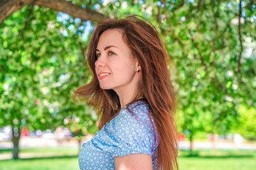 Portrait of a beautiful young woman in a blue dress in a blooming apple orchard in summer