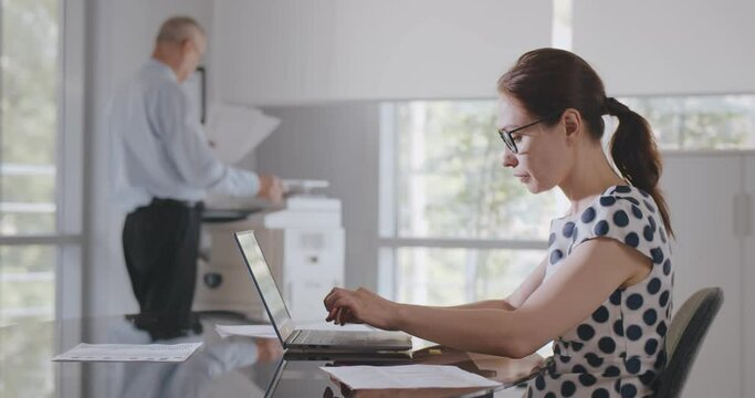 Side view of caucasian businesswoman sitting at desk in office using computer.