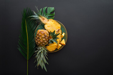 Sliced Pineapple on plate with tropical palm leaves. Bromelain whole pineapple summer fruit halves pineapple on black dark background. Summer fruit dessert. Top view Copy space - Powered by Adobe