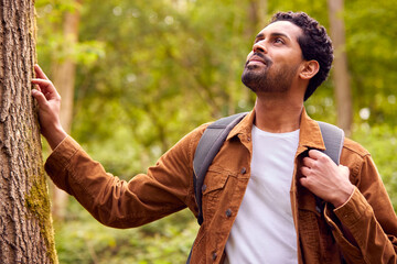 Man Hiking Along Path Through Forest In Countryside Taking A Break And Resting Against Tree