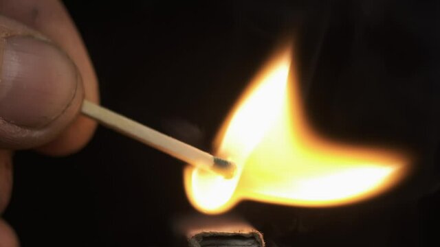 Slow motion. Ignition of a match by rubbing against a matchbox. Man blowing on a burning match and extinguishing the flame. Close-up