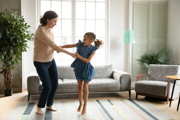Happy healthy old Caucasian grandmother and little granddaughter dance jump together in living...