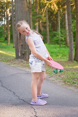 Cute little preteen girl posing with skateboard in beautiful park at sunny day.