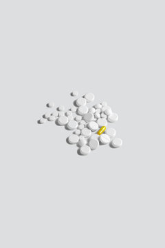 One yellow pill surrounded by white pills on gray background. The concept of medical treatment