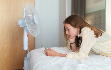 Teenager lies with the phone in front of cooling fan.