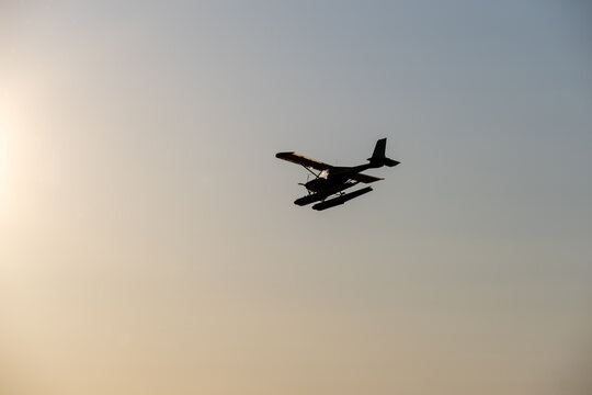 Silhouette of a small seaplane approaching the landing zone during the sunset.