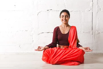 Tuinposter Young adult indian woman in sari meditating yoga lotus pose zen like with ok sign mudra gesture at home indoor. © primipil