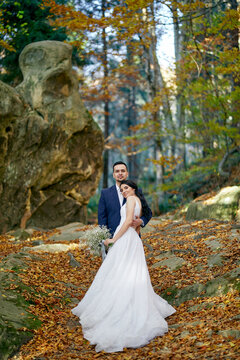 A groom and bride are embracing with beautiful background of mountains and trees. Autumn. Outdoor.