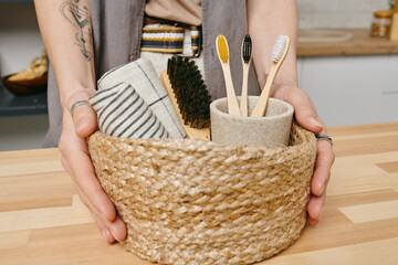 Hands of young healthy woman holding basket with rolled towels and brushes