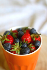 Cup of blueberries and strawberries on a bed. Selective focus.