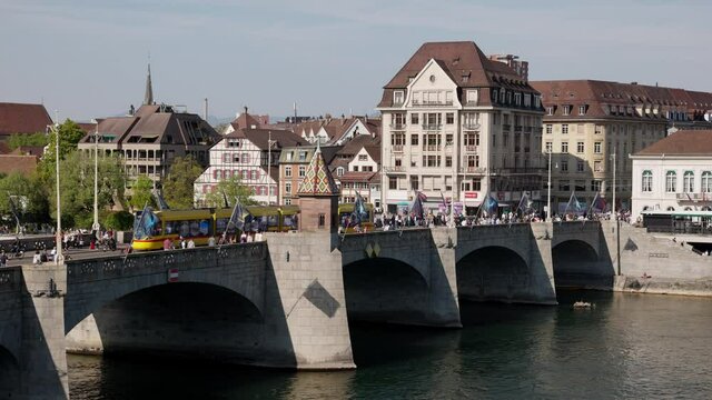 basel switzerland, 24 april. 2021: rhine bridge basel, filmed from the old town, yellow and green streetcar crossing the bridge, many people are out in the city in the afternoon