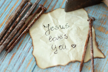 Jesus loves you. God's eternal love and forgiveness for humanity. Christ's sacrifice and atonement for our sins. Rusty nails and hammer with inspiring handwritten Bible quote. Biblical concept. - obrazy, fototapety, plakaty