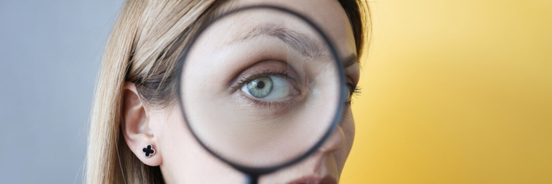 Young woman holding magnifying glass in front of her eye closeup