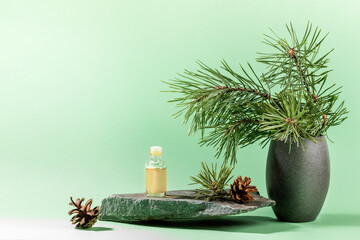 Composition with pine oil glass bottle, branches, cones on grey stone granite on mint green. Copy...