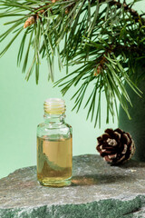 Essential pine oil in glass bottle on grey stone granite on mint green. Vertical orientation.