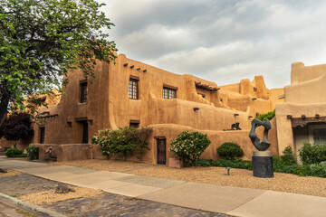 Fototapeta premium Pueblo Revival Style building with earth tone color, rounded corners and battered walls under dramatic cloudy sky, side, New Mexico Museum of Art, Santa Fe, New Mexico