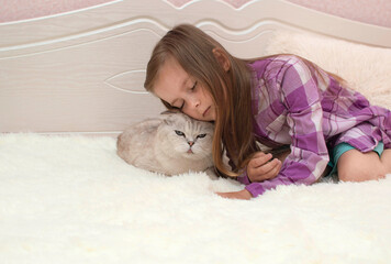A cute little child is lying on the bed, hugging a white cat and smiling, closing his eyes....