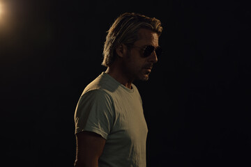 Man with blonde hair, a stubble beard and aviator sunglasses in a light green t-shirt. Side view.