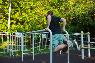 A guy in sports clothes does hand exercises on the uneven bars. Exercises for triceps on metal bars. A sports ground in the courtyard of the house for power loads. Blurred focus