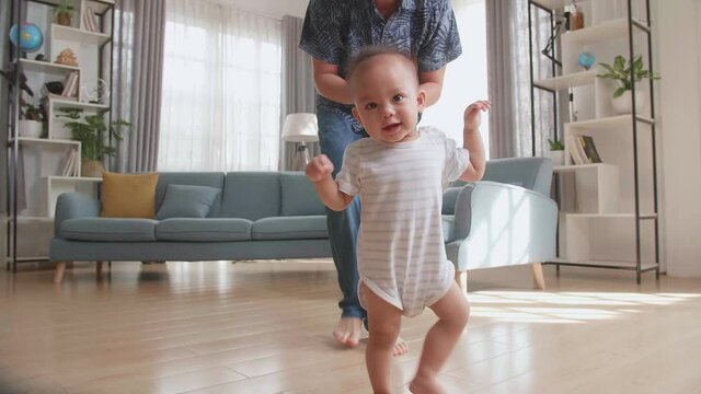 Father Encouraging Smiling Baby Son To Take First Steps And Walk At Home
