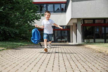 Happy boy running from school at the end of the school day with a backpack in hand. The beginning of the vacation.