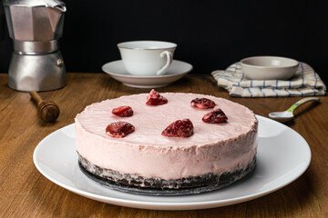 Side view of homemade delicious frozen strawberry cheesecake garnished with preserved dried strawberry in white ceramic dish.