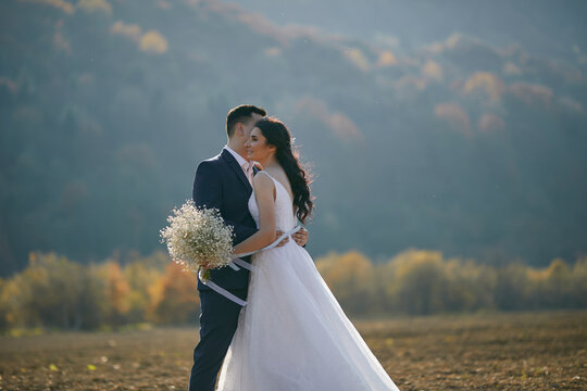 A groom and bride are hugging at the field with great view of hills. Outdoors. Nature