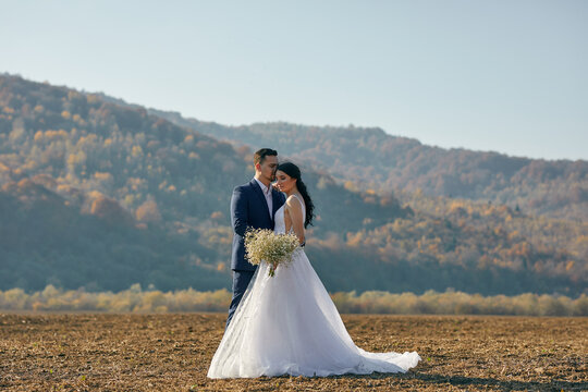 A beautiful young wedding couple embrace at the field with great view of hills. Outdoors. Nature